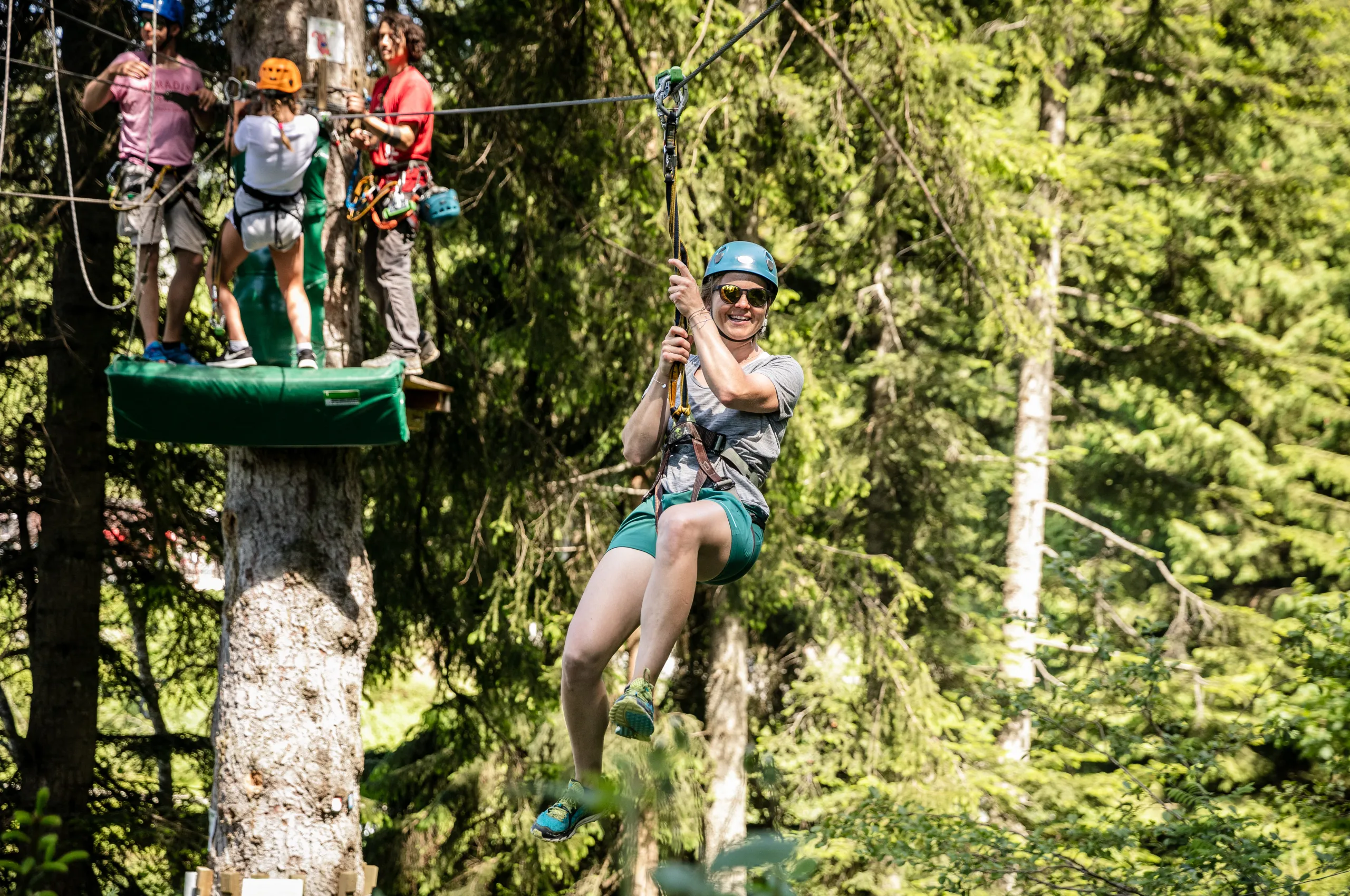 Person im Klettergurt schwingt an Seil durch Bäume